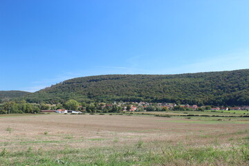 Beautiful French hilly landscape with a forest edge and a small village in the distance. Photo was taken on a summer day with blue sky.