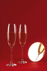 Two glassess of champagne with reflection in a small round mirror on a red background. Holiday and New Year concept. Copy space