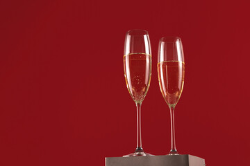 Two glassess of champagne on a stand on a red background. Holiday and New Year concept. Copy space