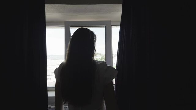 Woman silhouette with back pull aside the curtains, light coming in the dark, reveal hope