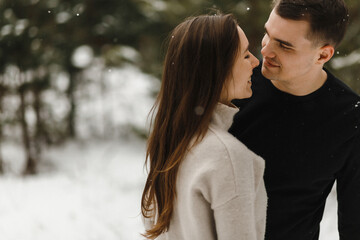 Fototapeta premium Young happy couple in love in the winter forest with copy space. Love, relationship, winter holidays. Winter couple photo ideas