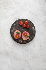 Two sandwiches with ham and cherry tomatoes and some greens on dark wooden cutting board on white textured background