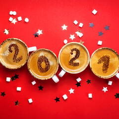 Figures 2021 as a symbol of the New Year on cups of hot aromatic coffee on a bright red background among stars and marshmallows. Top view, flat lay