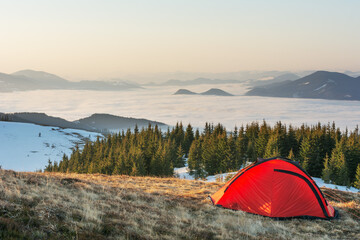 Spring on the mountainous valleys in the Ukrainian Carpathians overlooking the high snow-capped peaks covered with fogs against the backdrop of a tourist red tent