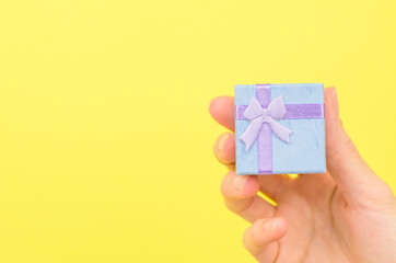 Small gift box in a female hand on a yellow background