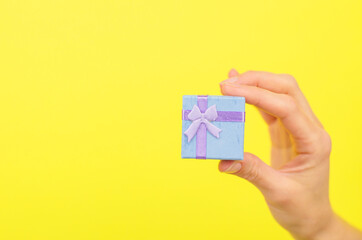 Small gift box in a female hand on a yellow background