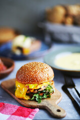 Fresh tasty hamburger among the food.Burger with beef, cheese, bacon and vegetables.Close-up burger with salad, cheese on the board.Classic burger.Food day.Food on the table.Spreading cheese