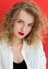 Young blonde woman with green eyes wearing white shirt over red background. Close up portrait of student curly girl. Beauty, fashion concept.