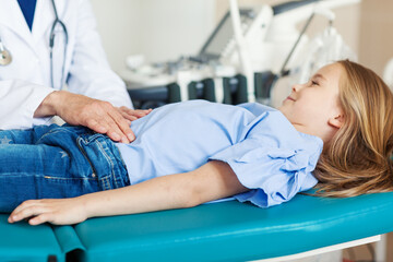 Unrecognizable doctor palpating belly of little girl lying on couch in doctors office and smiling