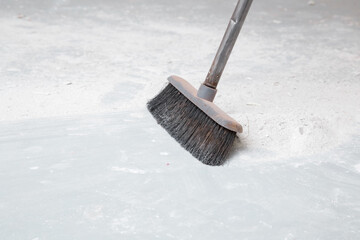 Broom sweeping white concrete dust from floor. Cleaning garbage after repair work of home. Closeup....