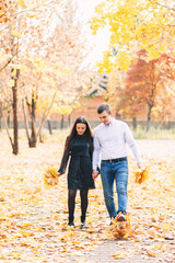 A loving couple walk on golden fallen maple leaves in the park in autumn