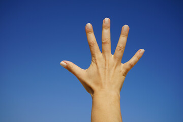 women's hands show the number five against a cloudless blue sky