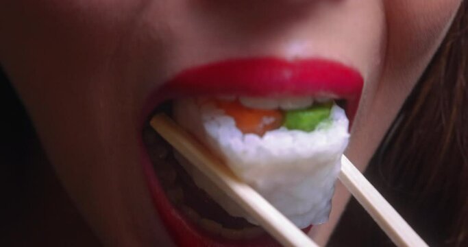 Young woman mouth eating sushi piece on chopsticks