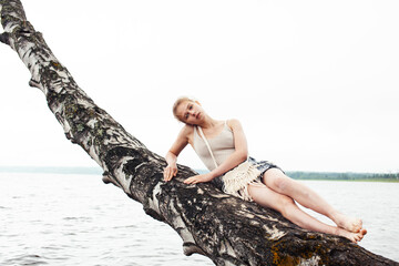 young blond woman hanging on birch tree at lake shore, summer vacations outdoor lifestyle