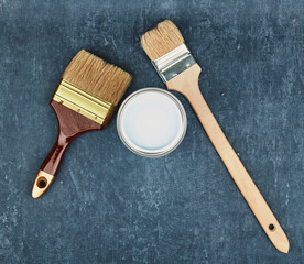 Two paint brushes and a closed can with white paint on a blue background, view from above