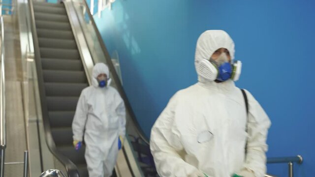 Disinfection service on escalator., team of sanitation workers in suit using pressure washer or sanitizer.