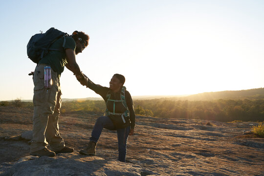 Man helps woman take step on mountain