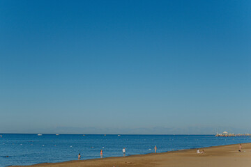 Small silhouettes of many people of different ages have fun on sunny summer tropical beach during summer vacations.