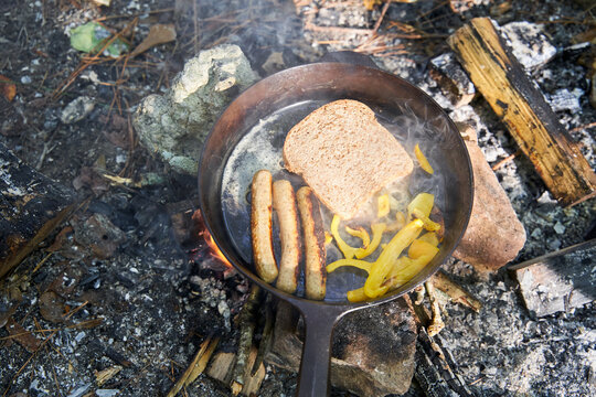 Breakfast being prepared over campsite fire in cast iron skillet