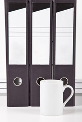 White coffee mug in front of folders at desk