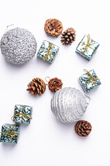 Fototapeta na wymiar Christmas New Year composition. Gifts, fir tree cones, silver ball decorations on white background. Winter holidays concept. Flat lay, top view