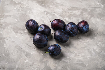Fresh ripe plum fruits with water drops on stone concrete background, angle view