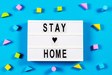 Stay at home. Lightbox with text STAY HOME and wooden toys blocks on blue background. Top view