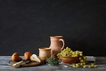 Still life in a rustic style: a set of clay dishes, grapes and pears on a wooden table. Natural...