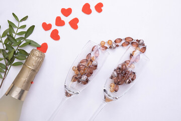 bottle of champagne, wine glasses, candies and hearts on a white background