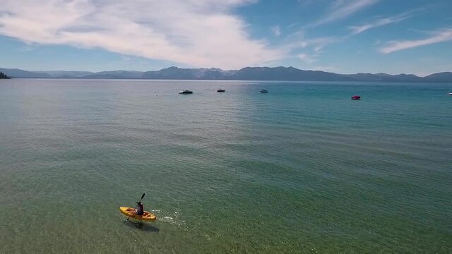 A woman in a yellow kayak paddles on the sunlight, crystal clear water of Lake Tahoe on a bright summer day.