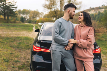 Beautiful couple talking and flirting leaning on their car