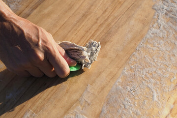 Crop image. Man surfer cleaning the surfboard from the old wax.