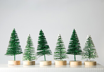 A group of small decorative Christmas trees on a white surface with a white background, a part with snow and a part without snow.Copy space, front view, layout.Greeting card,invitation design element.