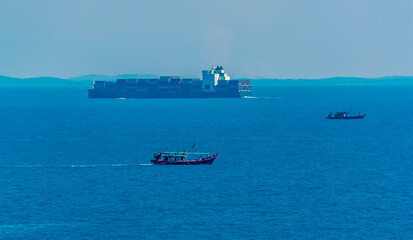 Traditional fishing boats mingle with large container ships in the Singapore Straits in Asia in summertime