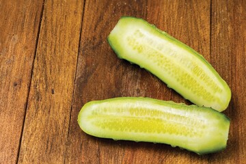 Close up view of cucumber cut in two parts on wooden background. Fresh vegetables and healthy eating concept.