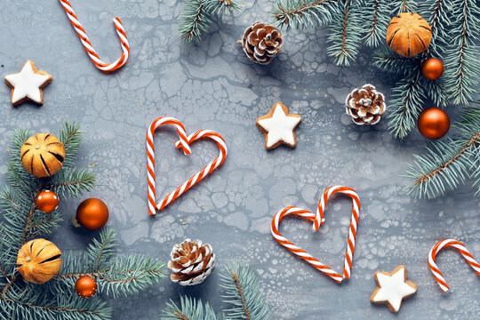 Grey textured Zero Waste Christmas background. Xmas flat lay, top view arrangement of natural fir twigs, dry oranges, pine cones and orange baubles. Heart shapes from stripy candy canes,