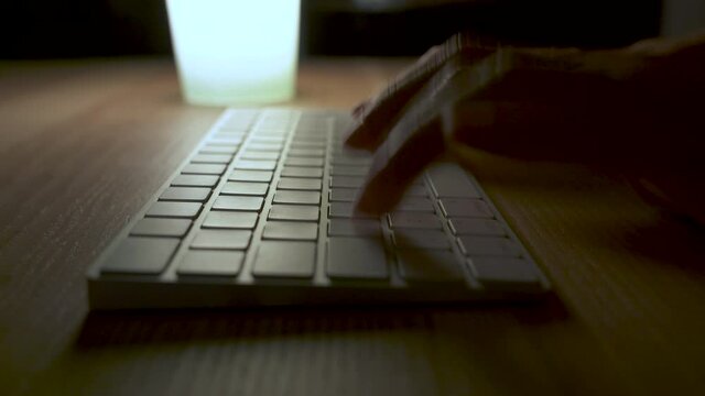 Woman typing on a wireless keyboard at night. Delete key.