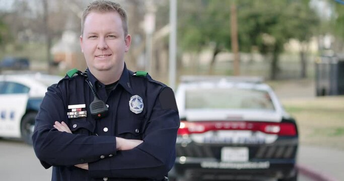 Police officer standing at police car with arms crossed