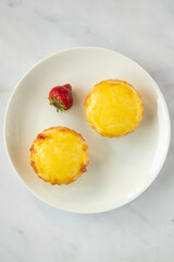 Two Hokkaido cheese tarts from japan on a plate in a top down view. with a strawberry