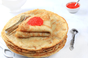 Delicious Russian pancakes with red caviar and a mug of milk on a bright light table. Healthy breakfast, natural products, traditional national cuisine, selective focus