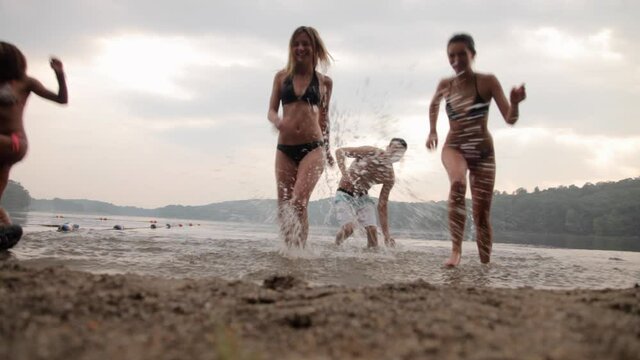Friends holding hands running from lake to shore