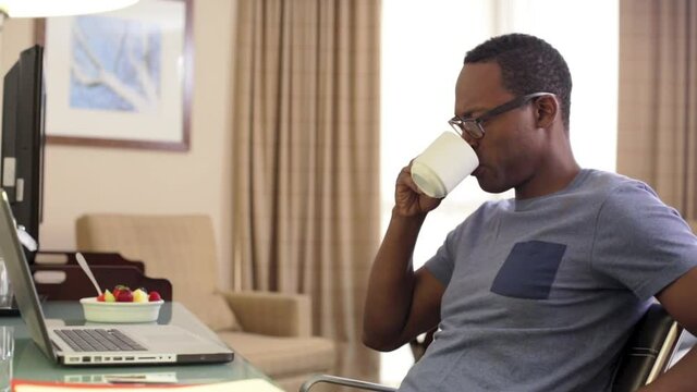 Black man drinking coffee and using laptop in hotel