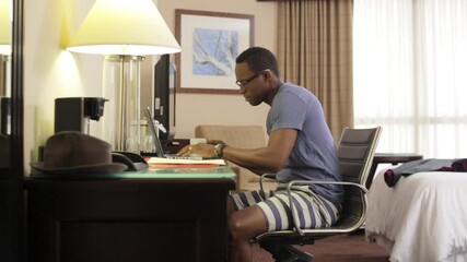 Black man drinking coffee and using laptop in hotel
