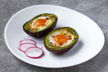 Baked eggs in avocado Boats with radish on white plate