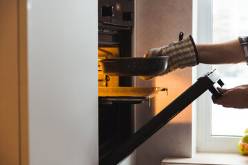 Man's hand in potholder puts mold with dish in the embedded oven in kitchen at home