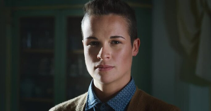Cinematic shot of an young attractive happy transgender man wearing formal elegant clothes is smiling in camera in a living room at home. Concept of gender expression, identity and diversity.