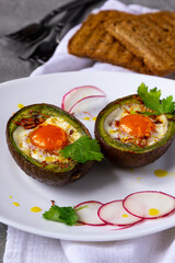 Baked eggs in avocado Boats with radish and toasts on white plate