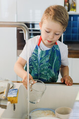 a boy in an apron washes dishes in the kitchen at home.