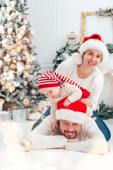 Fototapeta na wymiar Happy family under Christmas tree. baby boy in Santa Claus hat with gifts under Christmas tree with many gift boxes presents