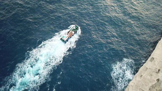 Fisherman boat moving near Maltese coast swinging on the waves lighted by evening sun. Boat moves toward the port visible at the distance. Aerial footage.